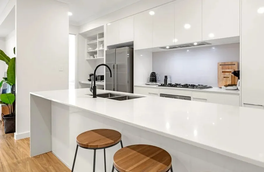 A white gloss kitchen with a waterfall island, black mixer tap and timber bar stools