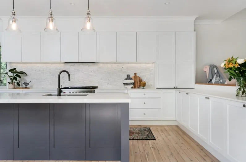A white shaker style kitchen with a charcoal shaker island, glass pendant lights and a marble mosaic splashback