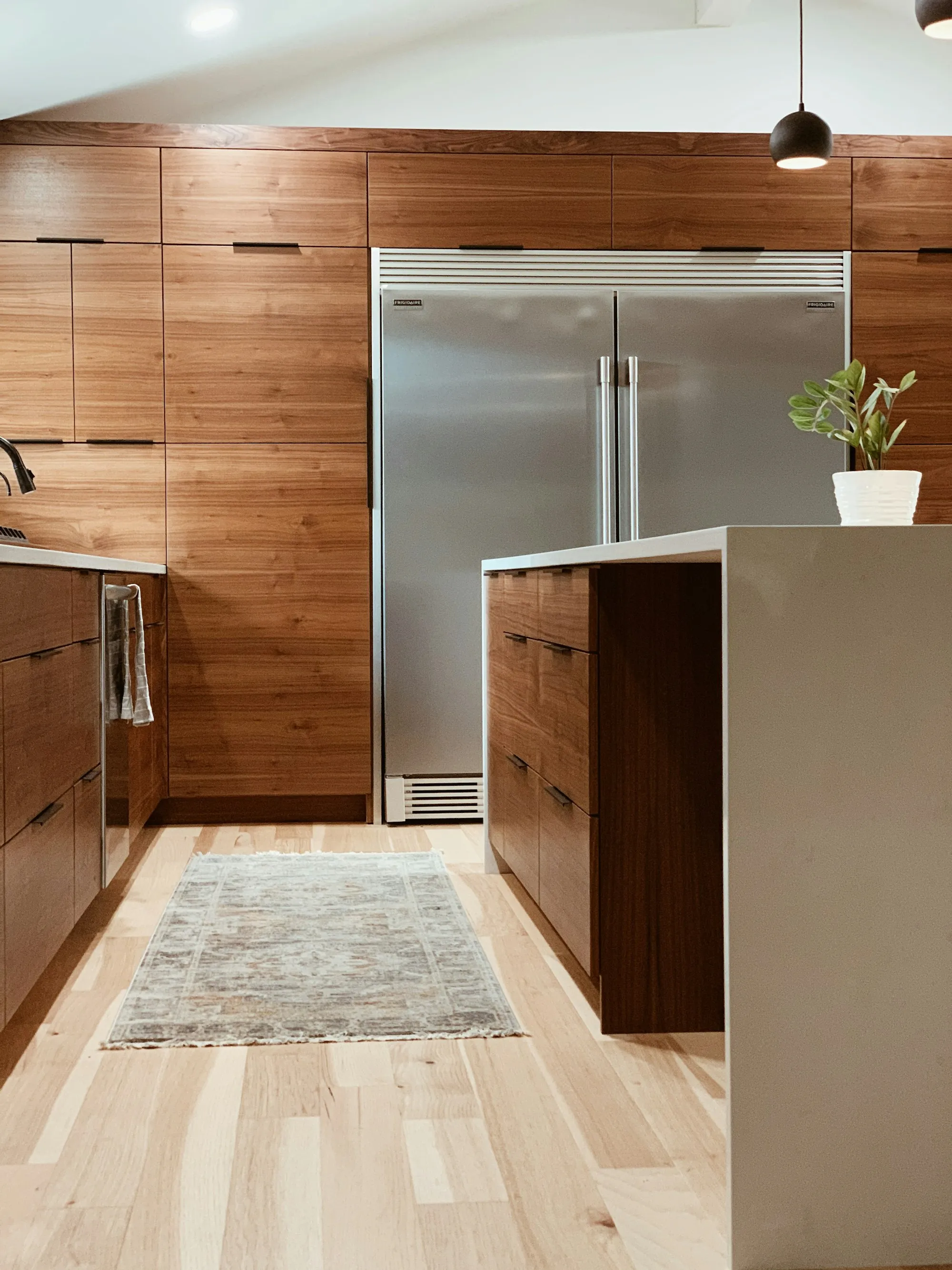 A kitchen with walnut look timber doors, a white stone island and integrated fridge