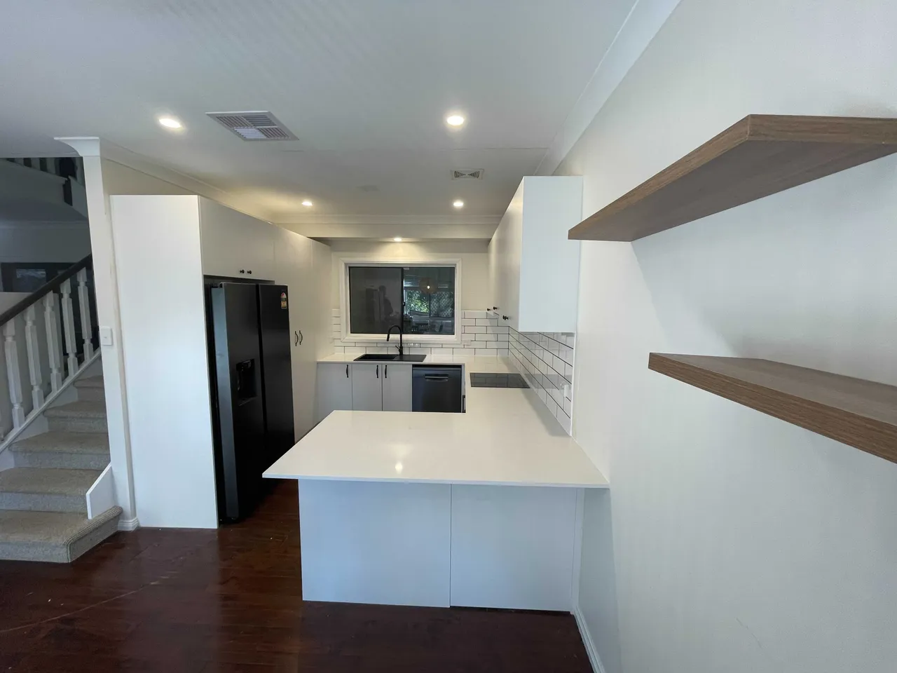 The same kitchen after, with a white stone benchtop, subway tiles and a black sink
