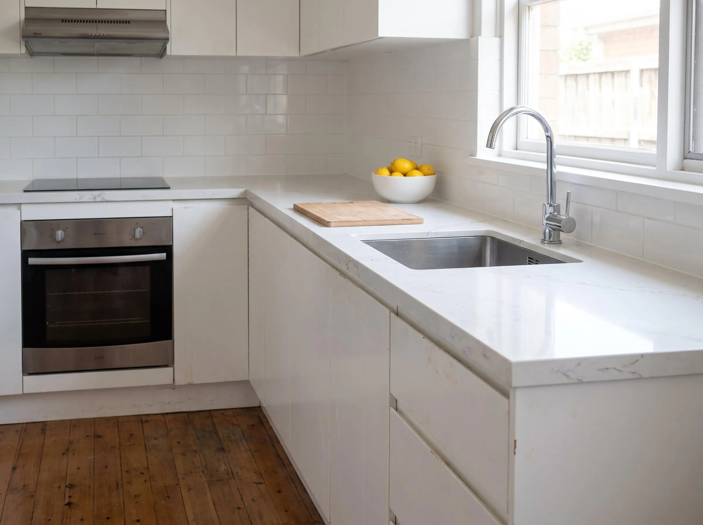 A white kitchen with a white stone benchtop, an undermount sink and timber floors